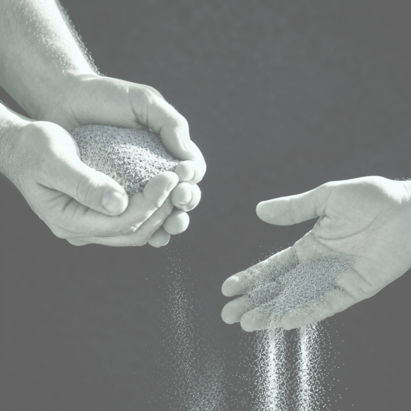 one person holding a handful of sand and another person letting the sand fall between their fingers.